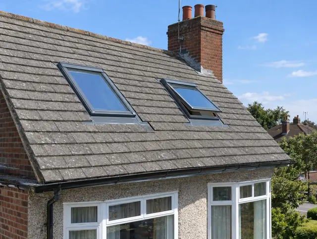 Two pitched roof windows with grey flashings in a tiled house roof